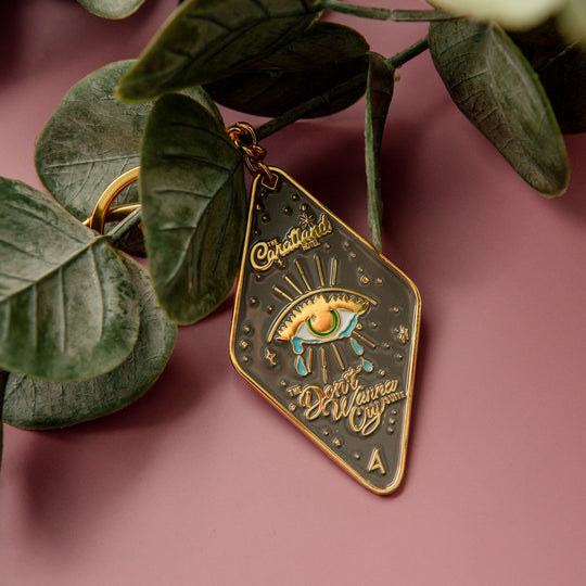 Decorative pendant with eye design and text on a pink background with green leaves